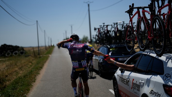 Tom Skujinš v 15. etape Tour de France berie fľaše s vodou z tímového auta a dáva si ich pod dres. 